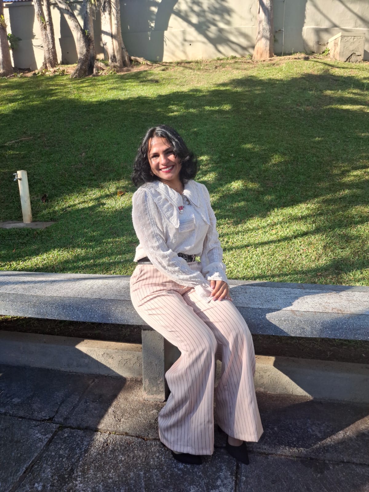 Irani Cristina sentada em um banco ao ar livre, usando blusa branca.